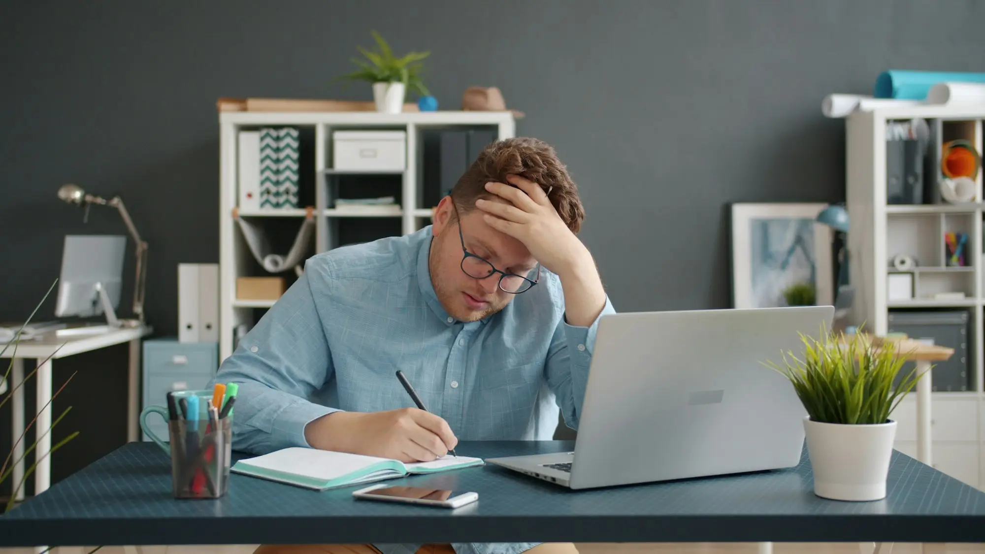 Stressed business owner writing at his desk in front of a laptop
