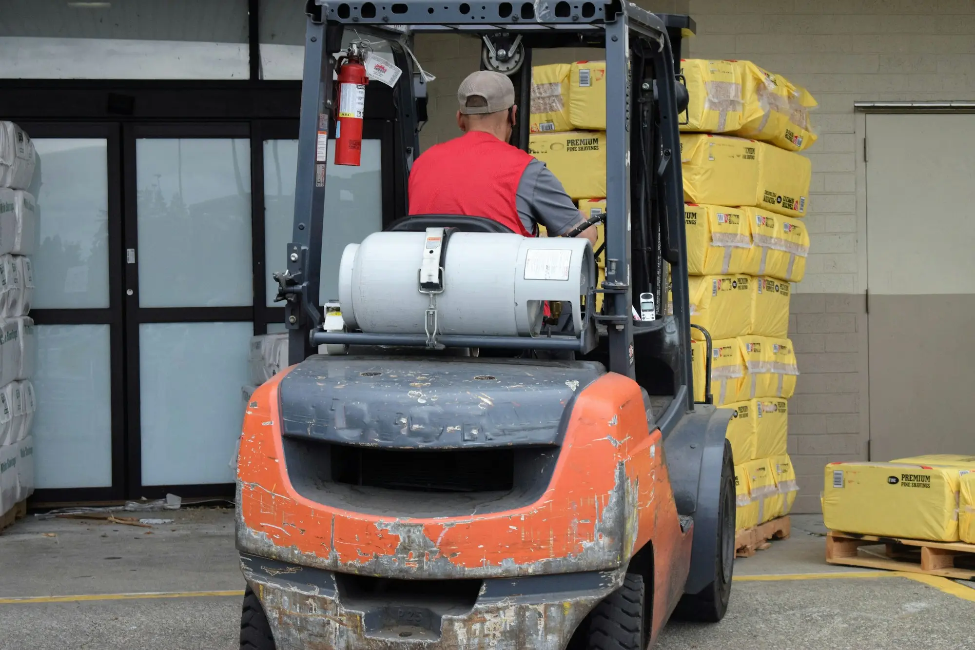 Worker driving a forklift between shelves of stock in a warehouse